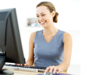 Woman in a blue vest laughing at a computer.