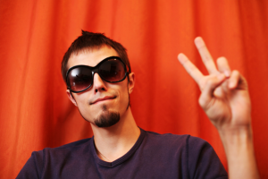 A man in sunglasses with a goatee beard posing in front of an orange curtain