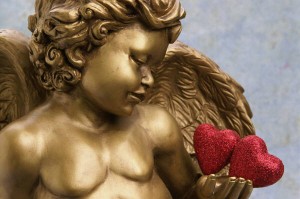 A gold coloured cupid holding two red hearts