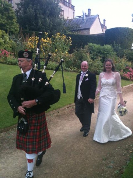 Photo of Nick and Lucy (who met on Muddy Matches) on their wedding day following a man playing bagpipes.