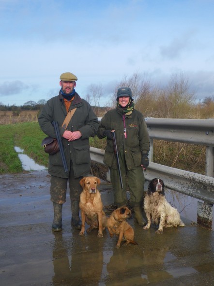 Man and woman in shooting gear with 3 dogs.